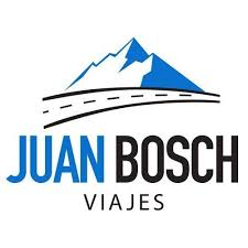 La imagen muestra el logo de una empresa llamada "JUAN BOSCH VIAJES". En la parte superior del texto, se observa un diseño estilizado de una montaña nevada de color azul y blanco, con una carretera curva de color negro y líneas discontinuas blancas que parece dirigirse hacia la montaña. Debajo de la imagen, en letras grandes y en negrita, se lee "JUAN BOSCH" con la palabra "JUAN" en color azul y "BOSCH" en color negro. Debajo de "JUAN BOSCH", en letras más pequeñas y de color negro, se encuentra la palabra "VIAJES".