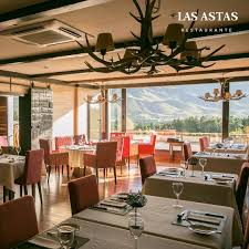 Las Astas - Interior del restaurante Astas, pisos, de madera, gran ventanal con vistas a la montaña y a la cancha de golf, mesas con manteles y sillas vestidas con telas con color suave rosado.