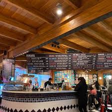 By the way I y II - Interior de restaurante de comidas rápidas, muy colorido, con pisos combinados en blancos con negros, mesas y sillas rojas y blancas, paredes turquesa.