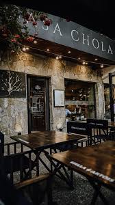 Casa Chola - Fachada de piedra, ventanales grandes, en la parte superior del frente el nombre del restaurante Casa Chola, en la vereda mesas y sillas de madera.