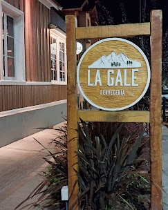 La Gale - Fachada de cervecería, con paredes de madera y ventanas blancas. Sobre la vereda el cartel de la marca La Gale.