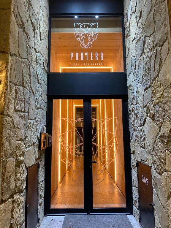 Pantera Bar Bistro - Entrada al restaurante Pantera Bistró, puerta de hierro color negro con grandes vidrios dibujados con el logo del comercio, paredes recubiertas de piedra.