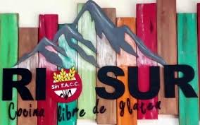 Rio Sur Sin Tacc - Logo con letras negras el símbolo sin tacc en el centro y detrás dibujada una montaña en gris.