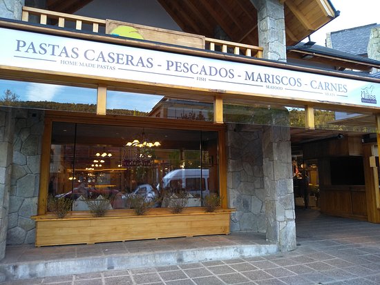 Ulises Restaurante - Fachada de restaurante con paredes recubiertas en piedra, gran ventanal de madera y en la parte superior el nombre de platos que ofrece.