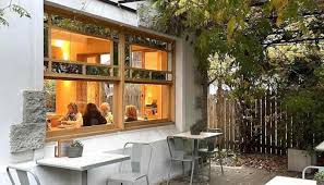 Almacén de Flores Bistro Bazar Andino Snowbrod - Fachada de la pastelería con paredes blancas una gran ventana de madera y en la vereda mesas y sillas blancas.