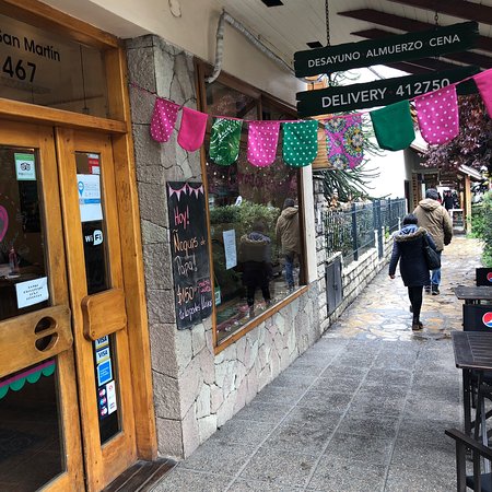 Corazón Contento - Imagen de la fachada de un restaurante, paredes cubiertas en piedra, puerta de madera, gran ventanal y banderines de colores colgados en la vereda.