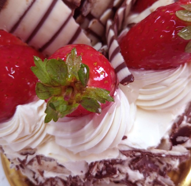 El Quijote - Una torta con crema, frutillas brillantes y trozos finos de chocolate blanco y negro sobre una bandeja dorada.