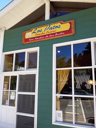 Los Patos - Fachada de comercio en forma de cabaña, con paredes de madera pintada de verde, ventanas y puerta con vidrios repartidos, techo a dos aguas y el cartel de Rotisería Los Patos.