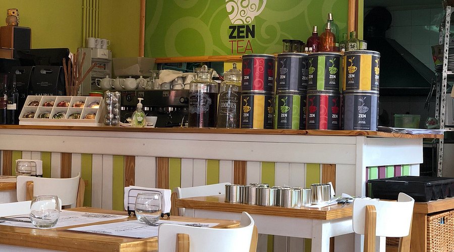 Zen Tea - Mostrador con productos de confitería y mesas y sillas blancas.