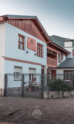 Casa de dos pisos con un estilo arquitectónico que combina elementos de madera y paredes claras. El techo es de dos aguas. Hay un cartel de madera tallado con un diseño de hoja o flor y la inscripción "RESIDENCIAL ITALIA" Es un lugar que da la impresión de ser pacífico y propicio para el descanso, quizás un retiro vacacional o un hogar en un entorno sereno.