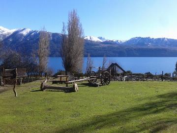 Imagen con una planicie de pasto verde, luego un lago de aguas azules y de fondo montañas con bosque y la cima nevada.