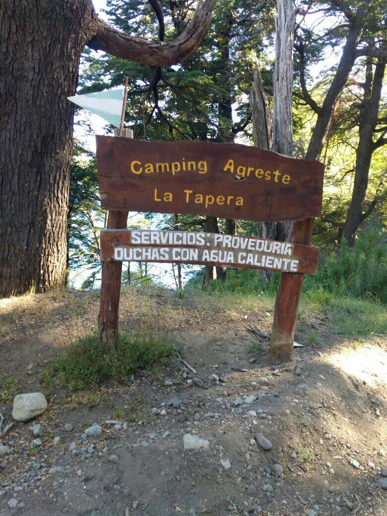 Imagen de un cartel de madera donde está escrito el nombre del camping La Tapera, detrás del cartel se observa el bosque.