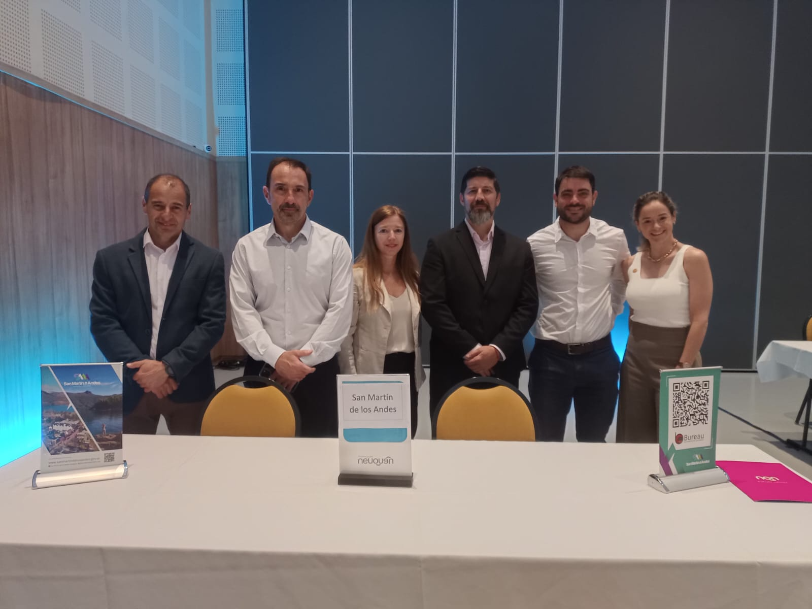 En la imagen se ve gente parada detras de un escritorio grande, con banners sobre la mesa. 