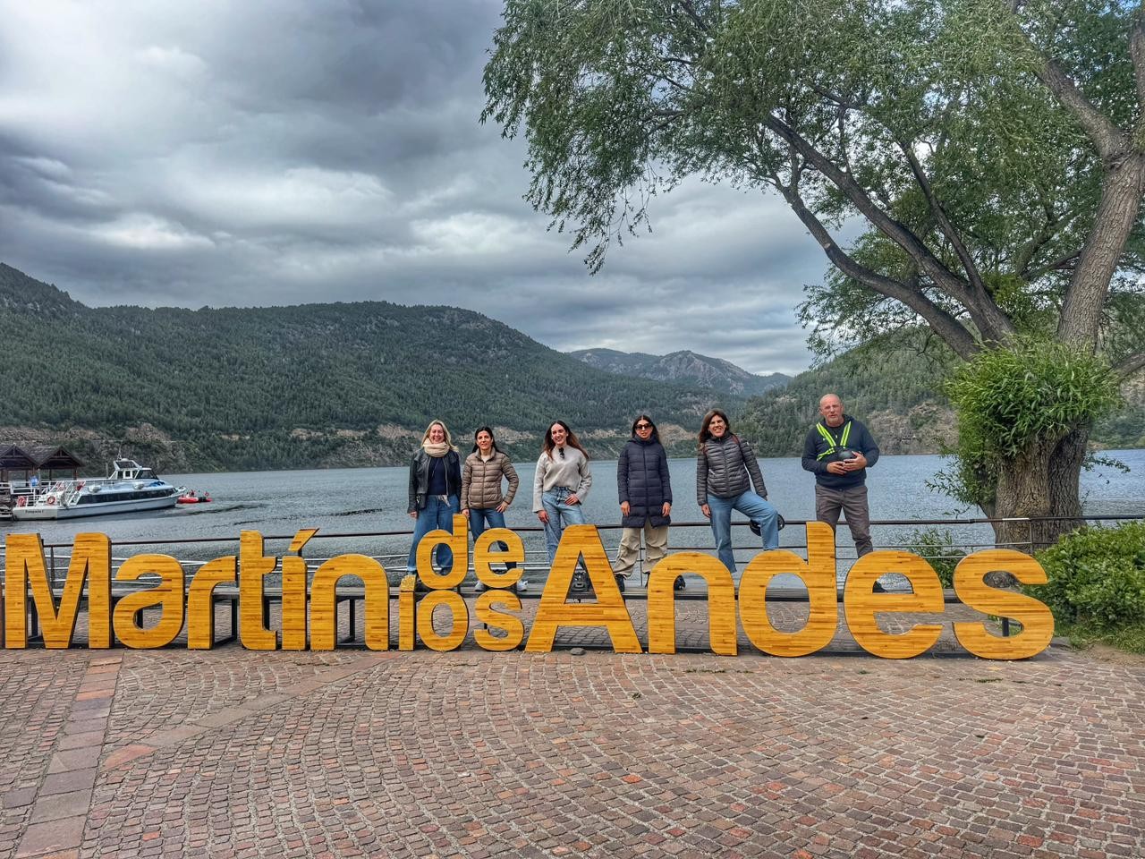 En la imagen se observan personas paradas detrás del cartel de San Martín de los Andes, de fondo un lago, montañas y vegetación.